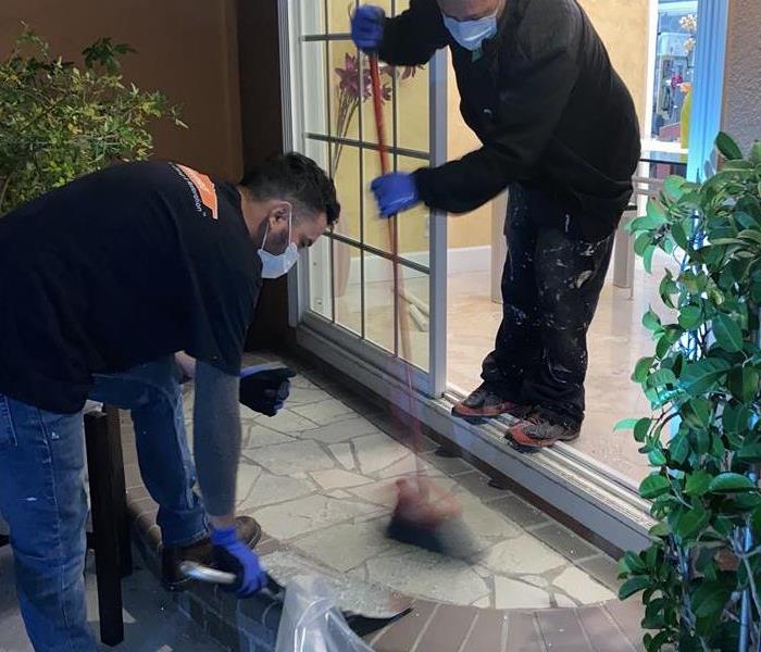 Two SERVPRO technicians cleaning up glass shards 