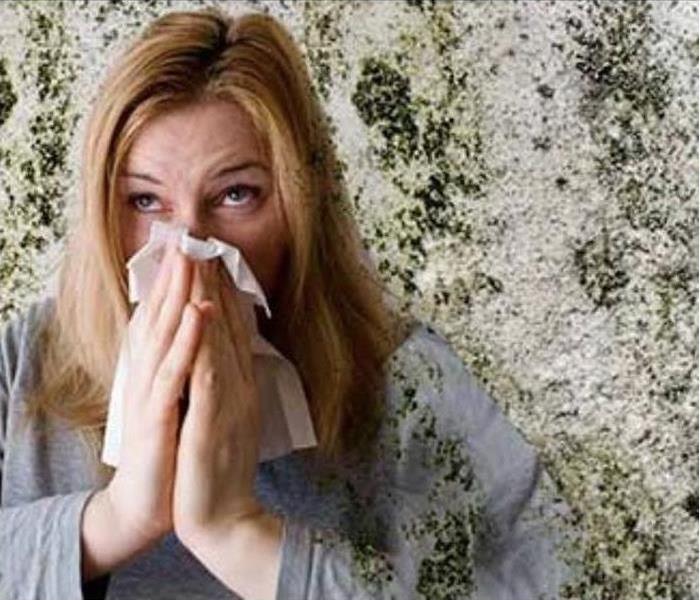 Woman blowing her nose into tissue, surrounded by mold 